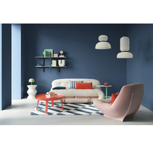 Wohnzimmer mit Sofa, Sessel, Teppich und Regalen an einer farbigen Wand