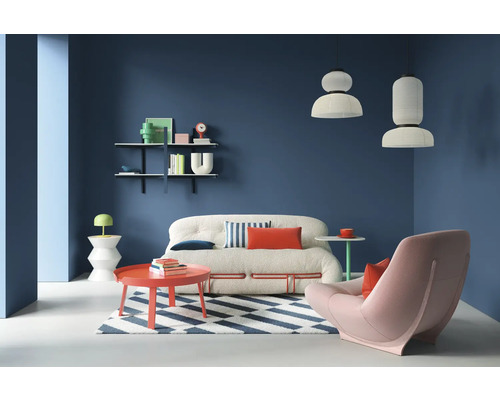 Wohnzimmer mit Sofa, Sessel, Teppich und Regalen an einer farbigen Wand