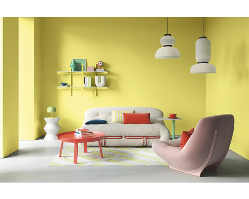 Wohnzimmer mit Sofa, Sessel, Couchtisch, Regalen und Pendelleuchten vor gelber Wand