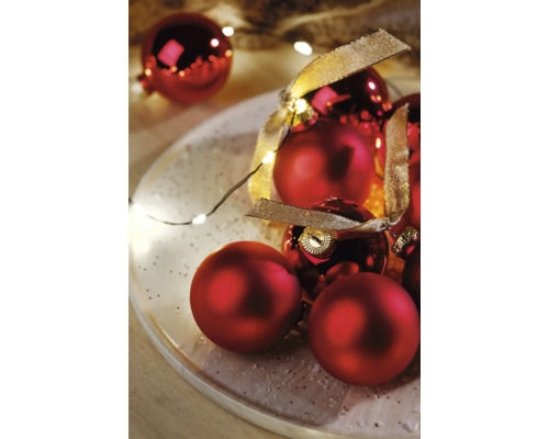 Rote Weihnachtskugeln mit Schleifenband auf einem Teller mit Lichterkette