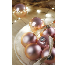 Dekorative Weihnachtskugeln mit Schleife auf einem Teller und Lichterkette