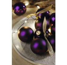 Dekorative violette Weihnachtskugeln mit Bändern auf einem Teller