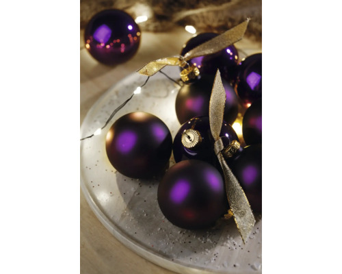 Dekorative violette Weihnachtskugeln mit Bändern auf einem Teller