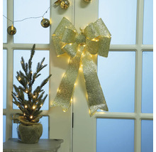 Dekorativer goldfarbener Schleifenbehang mit Beleuchtung und kleiner Tanne in Jutesack auf Tisch vor Tür