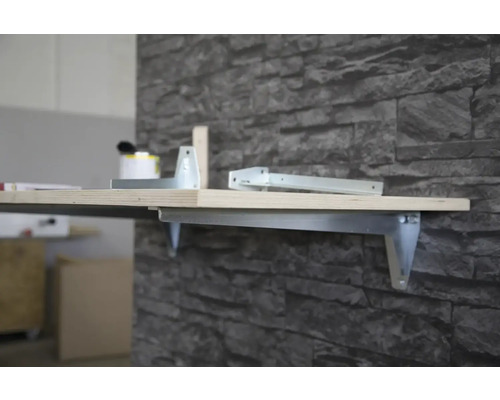 Wandregal mit Metallhalterung und Holzplatte an einer Steinwand