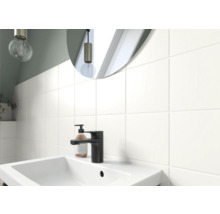 Badezimmerwaschtisch mit Armatur, Seifenspender und Spiegel vor einer gefliesten Wand