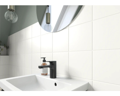 Badezimmerwaschtisch mit Armatur, Seifenspender und Spiegel vor einer gefliesten Wand