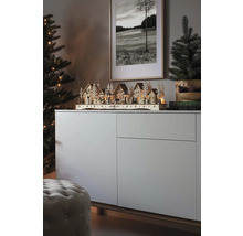 Weihnachtliche Szene mit einem beleuchteten Holzdorf auf einem Sideboard, neben einem Weihnachtsbaum und einem gerahmten Bild.