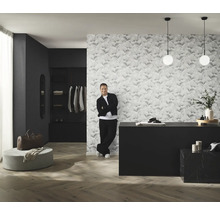 Raumansicht mit gemusterter Tapete, Kommode, Beleuchtung und Mann