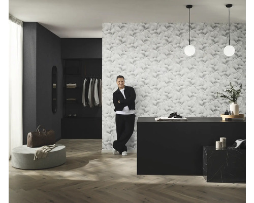 Raumansicht mit gemusterter Tapete, Kommode, Beleuchtung und Mann