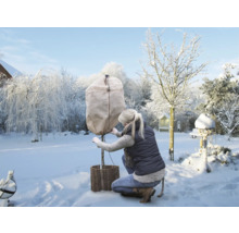 Frau schützt Baum mit Winterschutzhülle im verschneiten Garten.