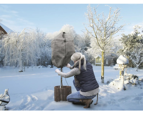 Frau befestigt Winterschutzhülle an Pflanze im Garten