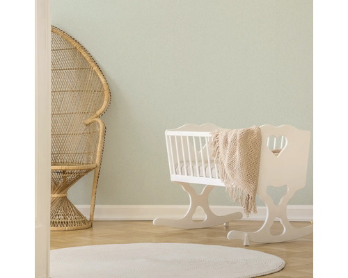 Helles Zimmer mit Korbstuhl, weißer Wiege und rundem Teppich.