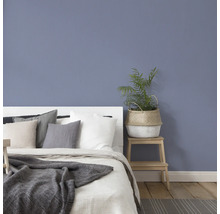 Schlafzimmer mit Bett, Kissen, Decke und Pflanze auf einem Hocker
