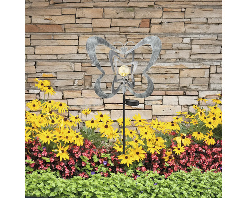 Dekorative Gartenleuchte mit Schmetterlingsmotiv und Solarpanel zwischen Blumenbeet