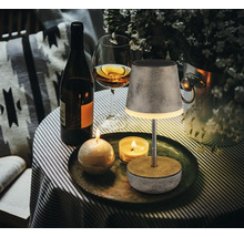 Dekoratives Tischarrangement mit Lampe, Flasche, Glas und Kerzen auf einem Tisch.