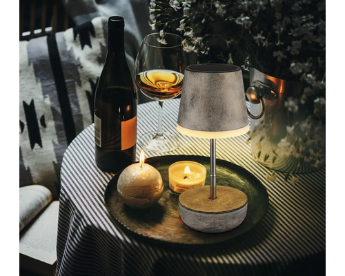 Dekoratives Tischarrangement mit Lampe, Flasche, Glas und Kerzen auf einem Tisch.