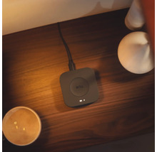 Philips Hue Bridge Smart Home Steuerzentrale auf einer Holzoberfläche bei warmer Beleuchtung, verbunden mit einem Kabel.