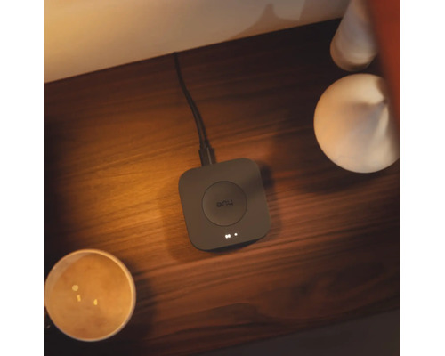 Philips Hue Bridge Smart Home Steuerzentrale auf einer Holzoberfläche bei warmer Beleuchtung, verbunden mit einem Kabel.