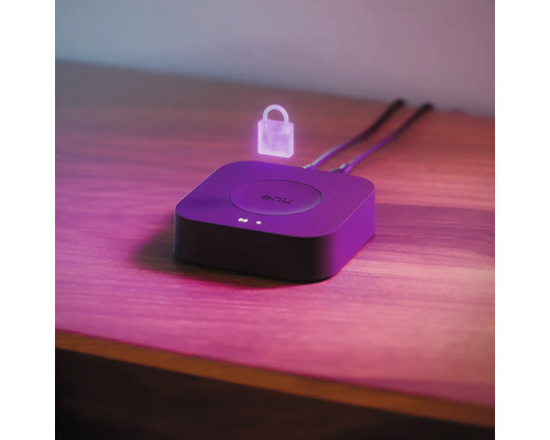 Philips Hue Bridge auf einer Holzoberfläche mit einem schwebenden Symbol für Sicherheit und zwei angeschlossenen Kabeln.