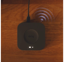 Quadratische Philips Hue Bridge Smart Home Zentrale auf einer Holzoberfläche mit visualisiertem Funksignal.
