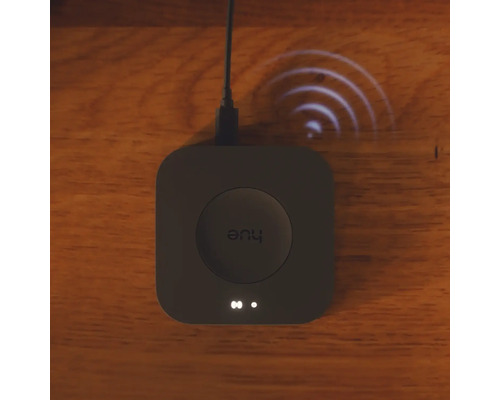 Quadratische Philips Hue Bridge Smart Home Zentrale auf einer Holzoberfläche mit visualisiertem Funksignal.