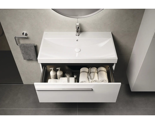 Modernes Badezimmerwaschbecken mit geöffneter Schublade, Handtüchern und Pflegeprodukten.