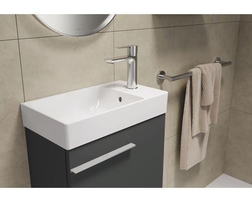 Badezimmer mit Waschtisch, Armatur, Handtuch und Spiegel für eine helle und organisierte Atmosphäre.