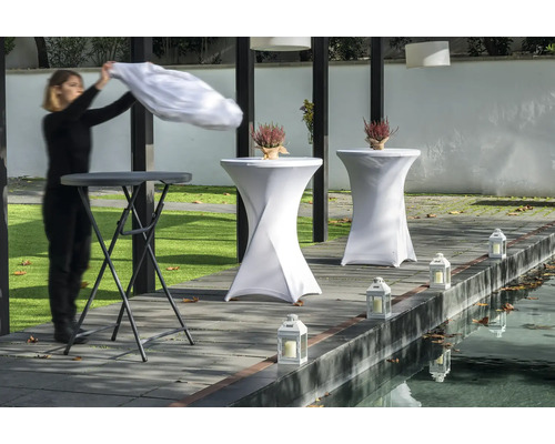 Szene mit Stehtischen, Tischhussen, Laternen und einer Person beim Auflegen eines Tuchs.