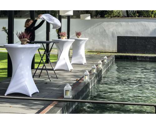 Szene mit Stehtischen, Blumendekoration und Laternen an einem Teich