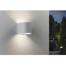 Eine zylindrische Wandleuchte strahlt Licht nach oben und unten an einer Wand ab.