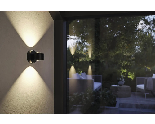 Dunkle Wandleuchte mit Lichtstrahlen nach oben und unten, die eine Gartenatmosphäre erhellt
