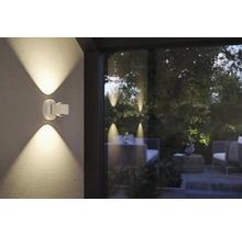 Eine moderne Aussenwandleuchte aus Metall beleuchtet eine Terrasse.