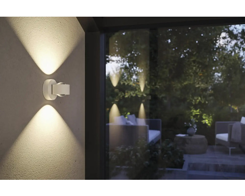 Eine moderne Aussenwandleuchte aus Metall beleuchtet eine Terrasse.