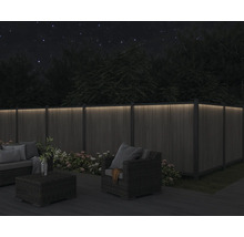 Eine Holzterrasse mit Lounge-Möbeln und einem beleuchteten Holzzaun bei Nacht.