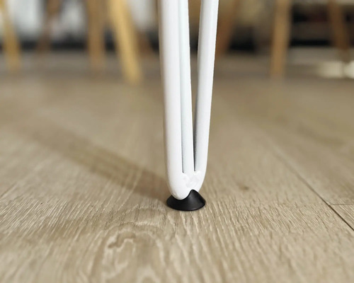 Detailaufnahme eines weißen Tischbeins mit Bodenschoner auf einem Holzboden.