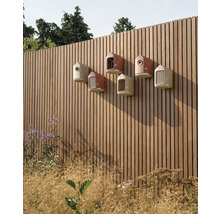 Verschiedene Vogelhäuser an einem Holzzaun in einem Garten.