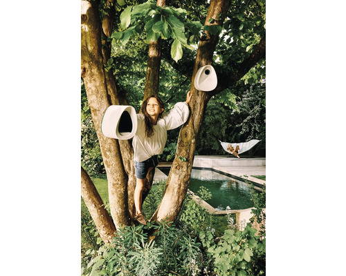 Mädchen klettert auf Baum mit Vogelhäusern im Garten