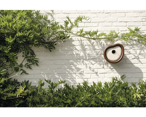 Modernes Vogelhaus an einer Backsteinmauer mit Pflanzen