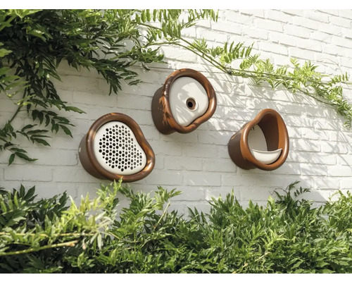 Drei verschiedene Vogelhäuser aus Keramik sind an einer Mauer befestigt.