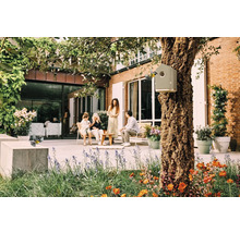 Szene im Garten mit Vogelhaus an einem Baum, sitzenden Personen und blühenden Blumen