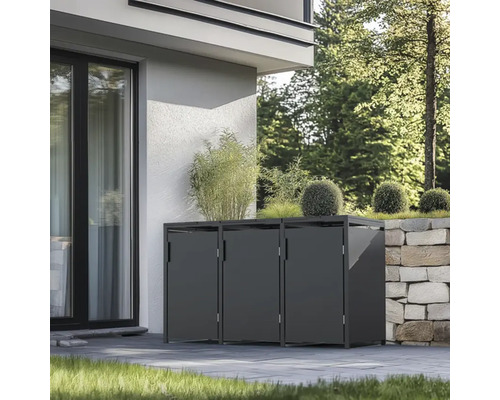 Drei Mülltonnenboxen vor einem Haus mit Pflanzen darauf und neben einer Steinmauer.