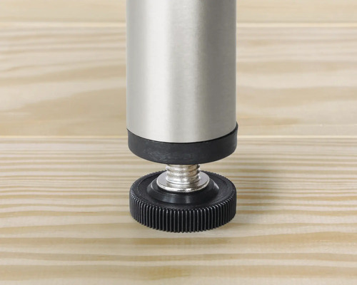 Detailansicht eines verstellbaren Möbelfußes aus Metall und Kunststoff auf einer Holzoberfläche.