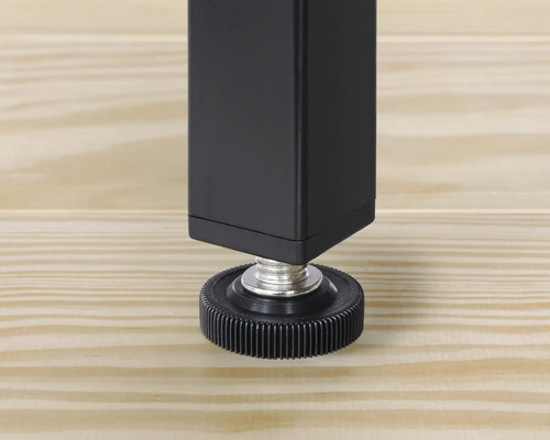 Detailansicht eines schwarzen Tischbeins mit Verstellfuß auf einem Holzboden.