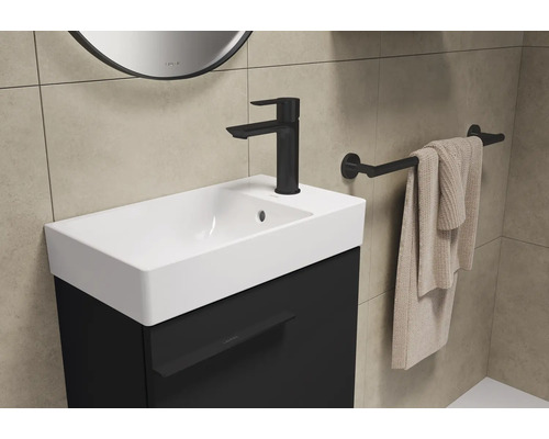 Waschtisch mit schwarzem Unterschrank, Armatur, Handtuchhalter und Handtuch in einem Badezimmer.