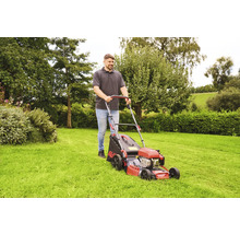 Ein Mann schiebt einen Rasenmäher auf einer Rasenfläche.