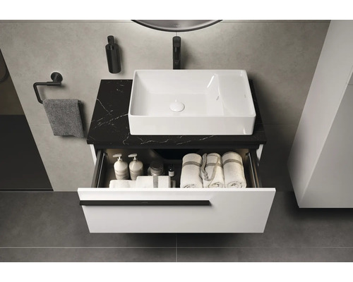 Badezimmer mit Waschbecken, Waschtisch mit Schublade, Handtüchern und Badutensilien.