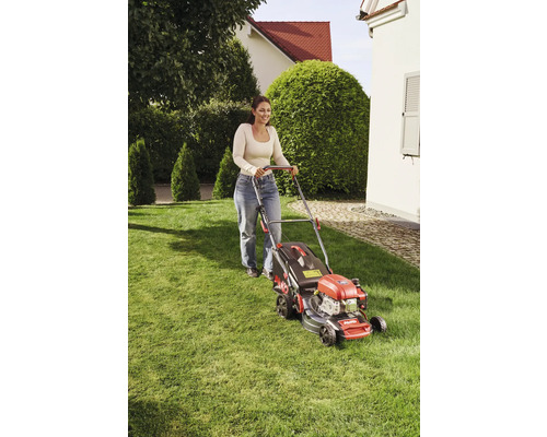 Frau bedient Rasenmäher im Garten.
