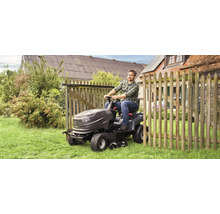 Ein Mann fährt einen Rasentraktor auf einer Rasenfläche neben einem Holzzaun.