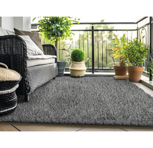 Balkonszene mit Rattansofa, Pflanzen und grauem Kunstrasen